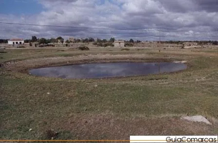 Charca en una llanura con casas al fondo