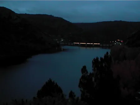 Embalse al anochecer con luces lejanas
