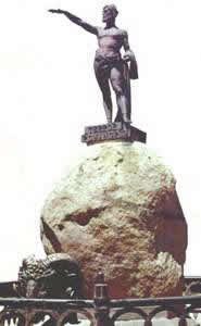 Monumento con una figura masculina de bronce de brazo extendido sobre una gran roca